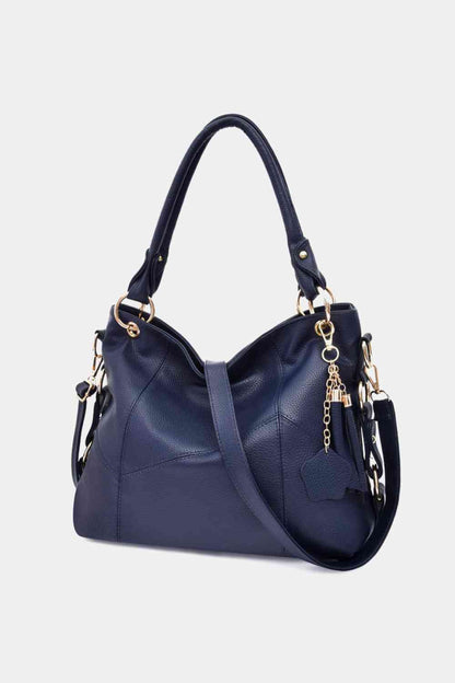 the front of the bag where the 3 different style of tassels shows at the front. a pu leather strap that you can wear on the side or crossbody. the bag is a navy blue with gold metals design. 